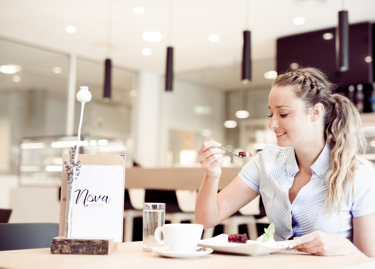 Dame sitzt im NOVA-das Café an einem Tisch und isst gerade ein Stück Kuchen.