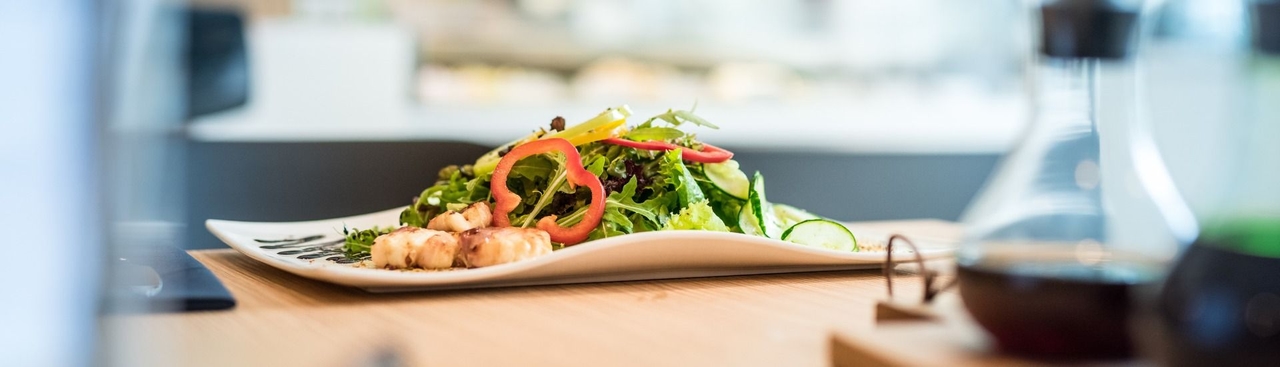Teller mit grünem Salat, Paprika und gegrilltem Schafkäse im Speckmantel.