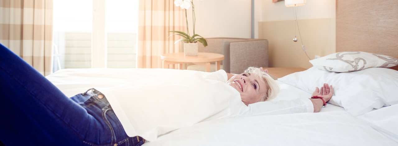 Dame liegt im Hotelbett und lächelt. 