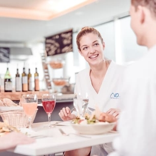 Pärchen im Thermenrestaurant: beide sitzen am Tisch und essen, Die Dame lacht den Herrn herzlich an.