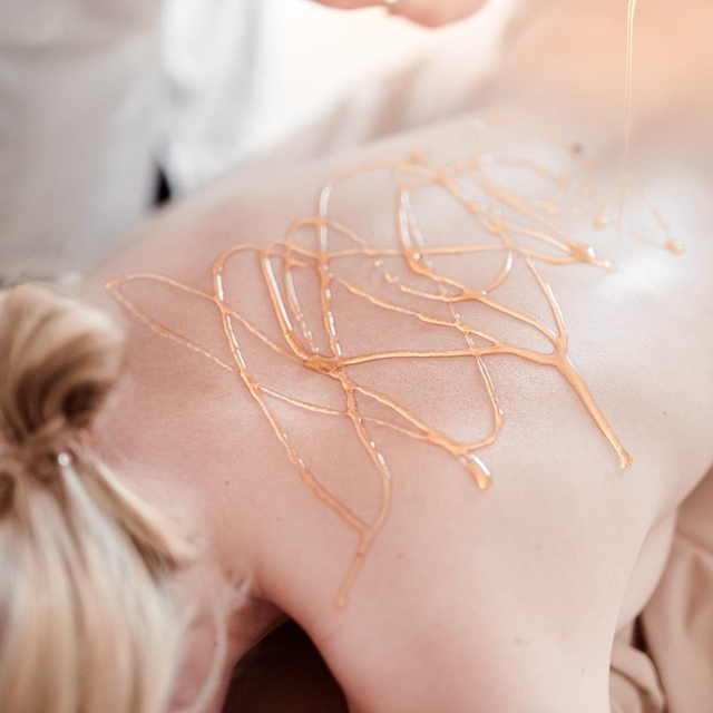 Honigmassage: Dame liegt am Bauch, ihr Rücken ist mit Honig beträufelt. 