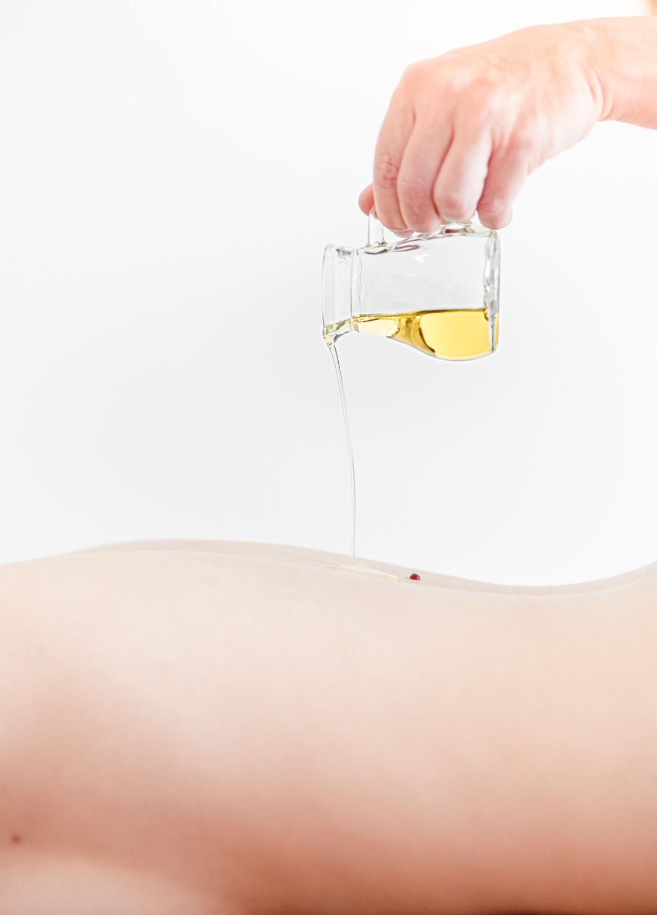 Dame liegt am Bauch, während ihr gerade Massageöl am Rücken aufgetragen wird.