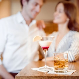 Im Vordergrund sind zwei Drinks zu sehen und dahinter ein Pärchen das sich anlacht.