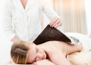 Dame Liegt nackt am Bauch während eine Masseurin die Moorpackung am Rücken anbringt.