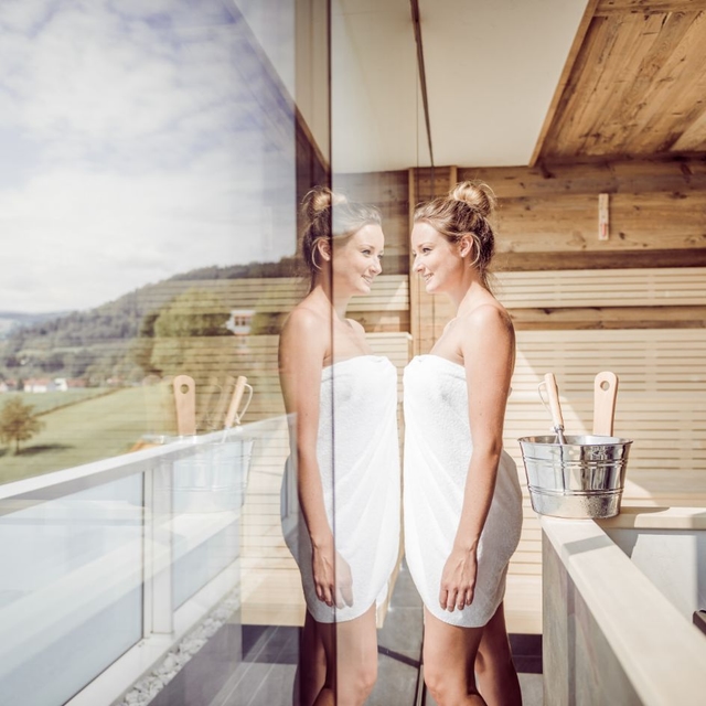Dame mit Badetuch steht an der Glasfront der Stubalmsauna der Therme NOVA und blickt nach außen.