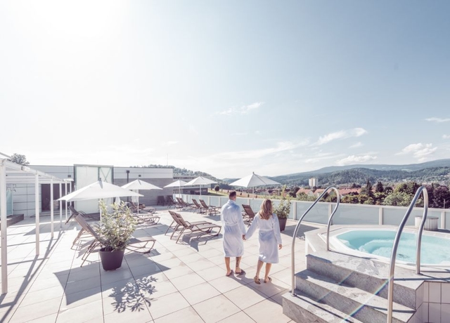 Pärchen im Bademantel steht am Saunadach der Therme NOVA und blickt auf die umliegende Landschaft.