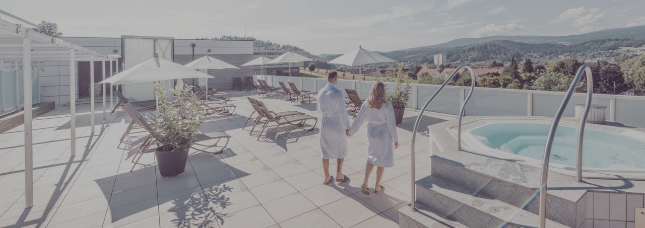 Pärchen im Bademantel steht am Saunadach der Therme NOVA und blickt auf die umliegende Landschaft.