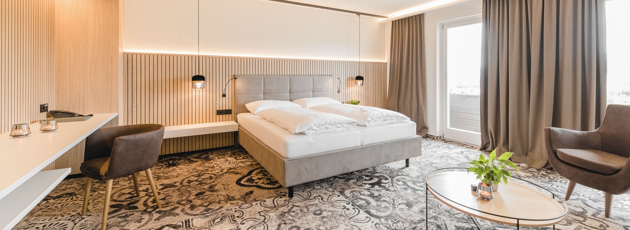 Blick in die Junior Suite vom Hotel NOVA. Zu sehen ist ein Doppelbett, ein Schreibtisch inkl. Stuhl und die Balkontüre.