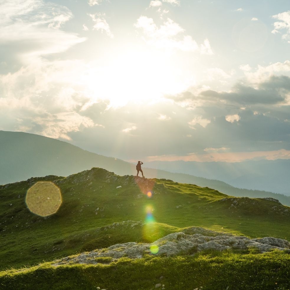 Person steht auf einem Hügel und blickt auf die umliegende Landschaft.