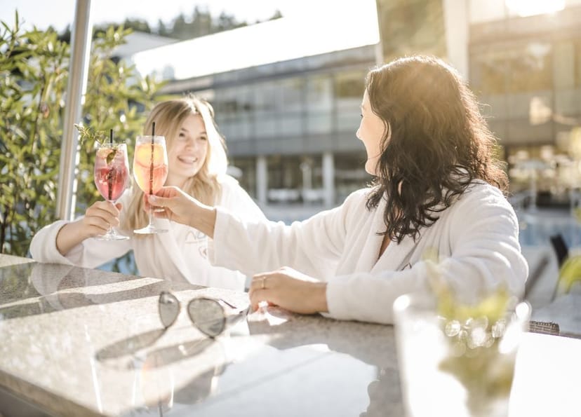 Zwei Damen sitzen an der Bar in der Therme NOVA und stoßen mit rötlichem Getränk an.