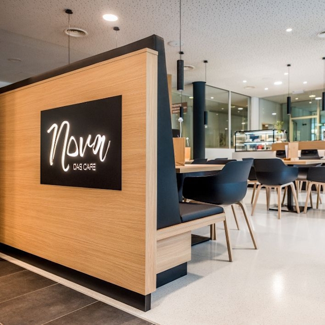 Eingangsbereich NOVA-das Café. Zu sehen ist eine Sitzbank und das Logo.