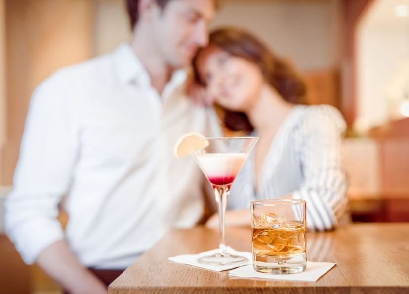 Im Vordergrund sind zwei Drinks zu sehen und dahinter ein Pärchen das sich anlacht.
