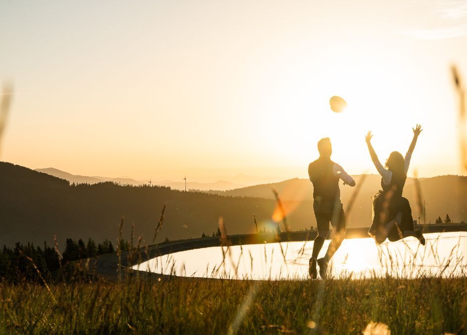 Pärchen springend vor einem See im Morgengrauen.