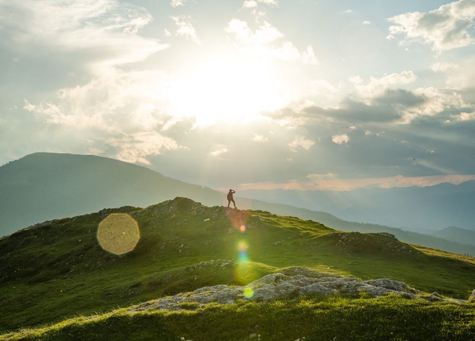 Person steht auf einem Hügel und blickt auf die umliegende Landschaft.