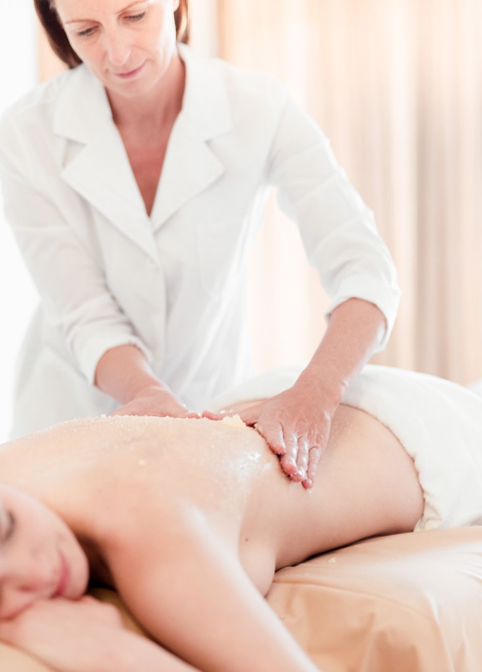 Eine Masseurin massiert den Rücken einer am Bauch liegenden Dame.