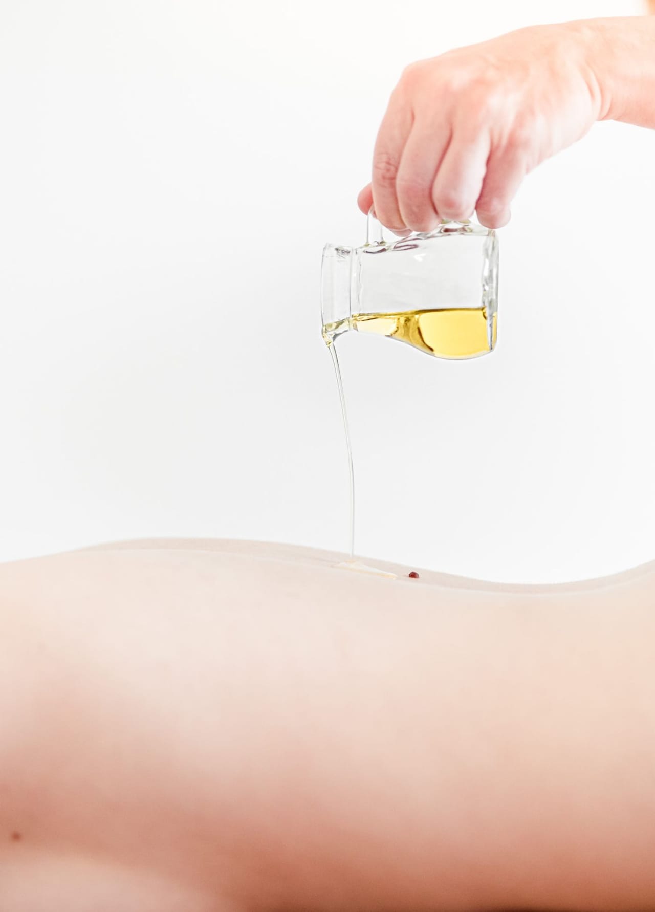 Dame liegt am Bauch, während ihr gerade Massageöl am Rücken aufgetragen wird.