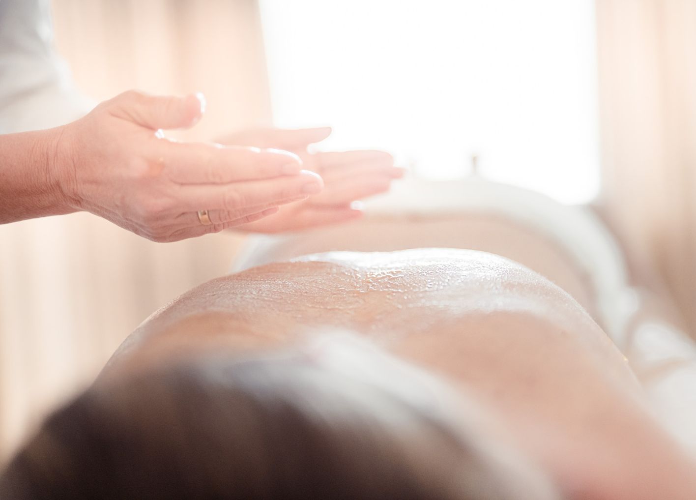Zu sehen ist der Rücken einer Dame, darüber die Hände des Masseurs kurz bevor er mit seiner Massage beginnt.
