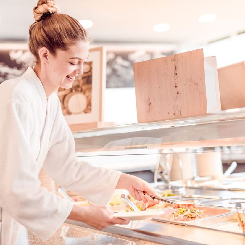 Junge Dame am Buffet. Sie ist gerade dabei ein Gericht auf Ihren Teller zu geben.