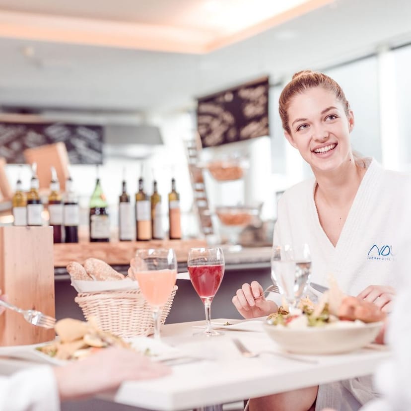 Junge Dame sitzt an einem Esstisch des Thermenrestaurants der Therme NOVA und lächelt.