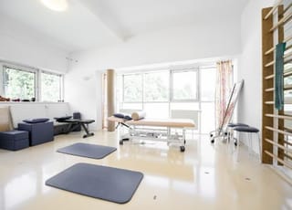 Blick in den Gymnastikraum für die Einzelheilgymnastik. Zu sehen ist eine Liege, Trainingsmatten sowie eine Sprossenleiter.