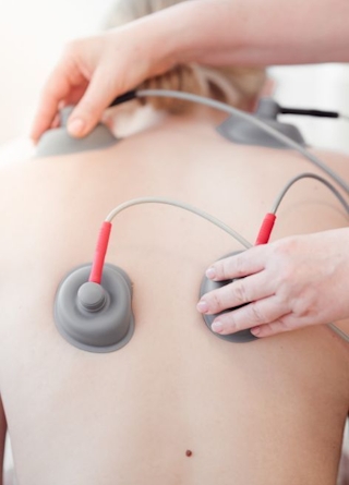 Zu sehen ist der Rücken einer Dame auf den Elektroden-Knöpfe der Elektrotherapie angebracht sind. 