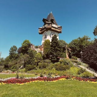 Blick auf den Uhrturm von Graz. Davor ein schön angelegter Garten.