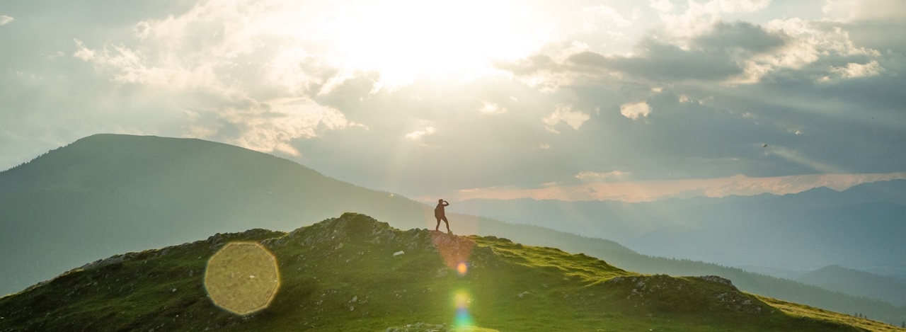 Person steht auf einem Hügel und blickt auf die umliegende Landschaft.